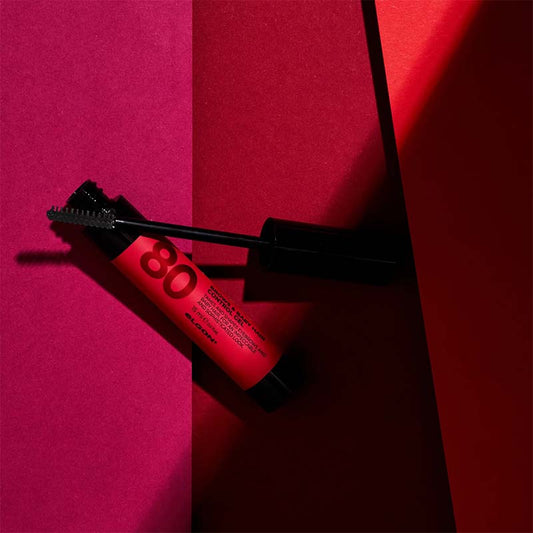 Flacone nero con etichetta rossa aperto su sfondo rosso.