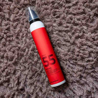 Flacone bianco con etichetta rossa con scritte nere ed erogatore nero con cappuccio trasparente steso su un tappeto marroncino.